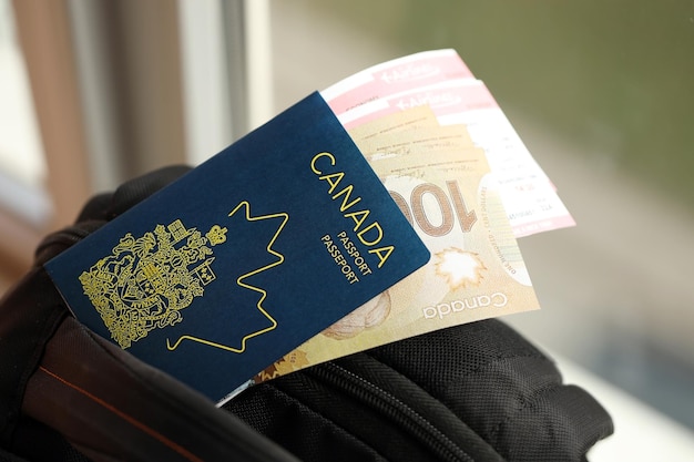 Canadian passport and dollar money bills with airline tickets on backpack close up