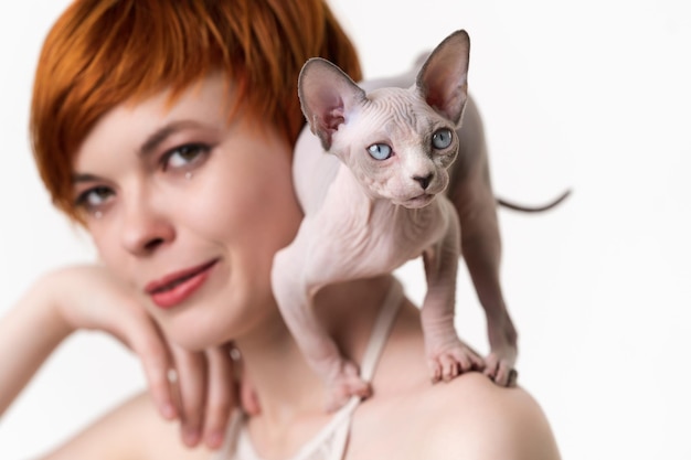 Canadian Sphynx Cat standing in defensive pose on shoulder of redhead young woman with short hair