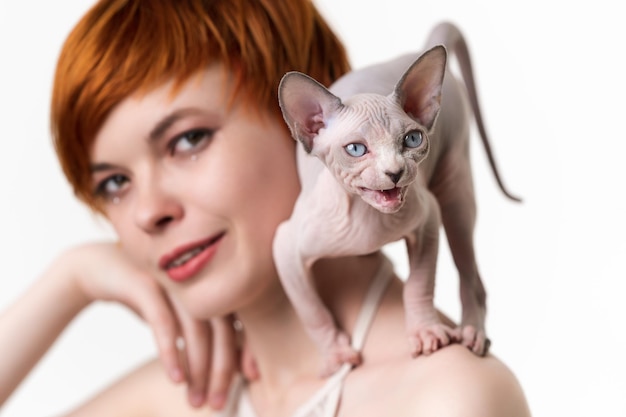 Canadian Sphynx Cat stands in defensive posture and meows on shoulder of redhead young woman