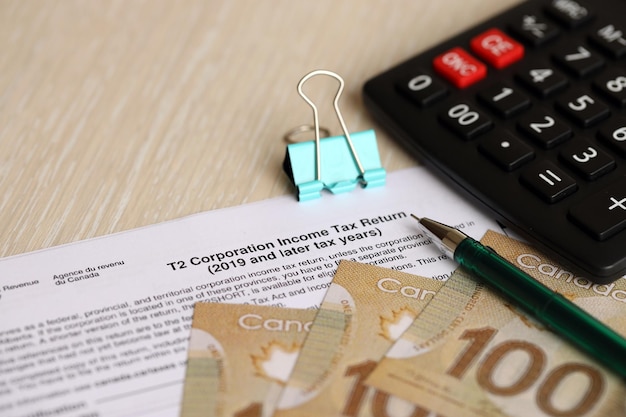カナダの税務フォーム 会社の所得税の申告書は,カナダの紙幣と一緒にテーブルの上にあります.