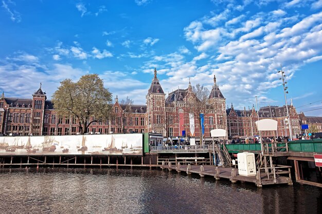 Canal at open havenfront in amsterdam, netherlands. centraal train station and people on the background