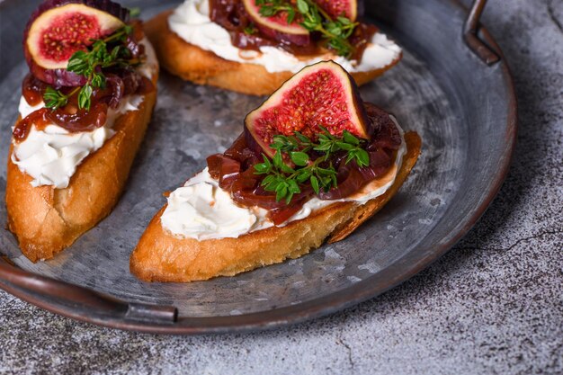 Canape or crostini with toasted baguette cream cheese onion jam figs and  thyme on a tin tray