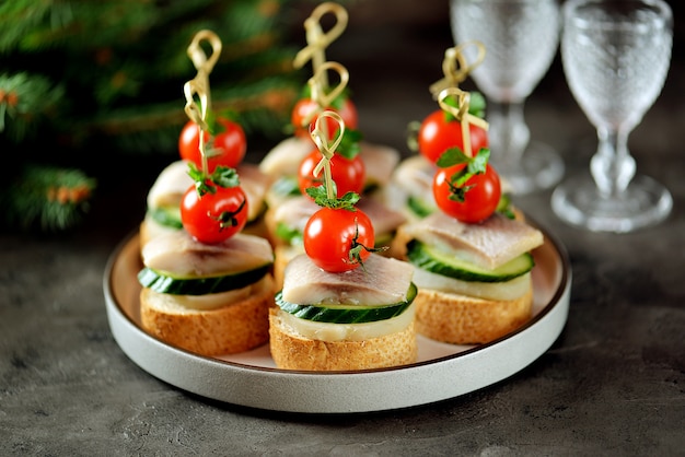 Canape with salted herring, cucumber, boiled potatoes and cherry tomato on croutons