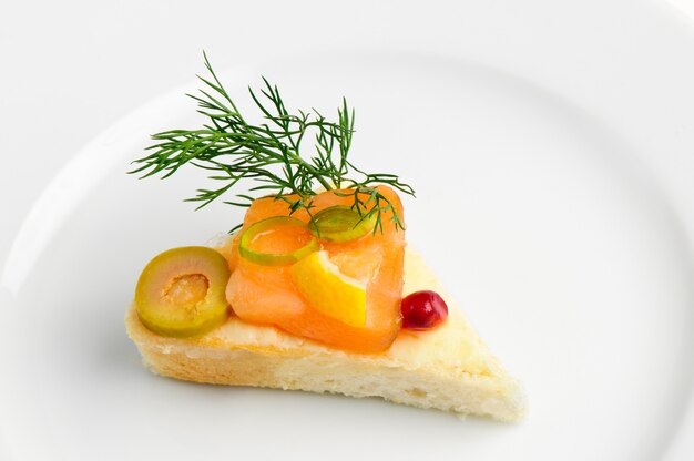 Canape with slice of smoked salmon, green olive, dill and seed of pomegranate