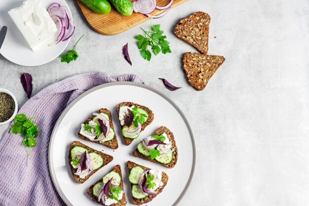 Canapeetjes met geroosterd brood met zonnebloem- en lijnzaad, fetakaas, komkommer en ui