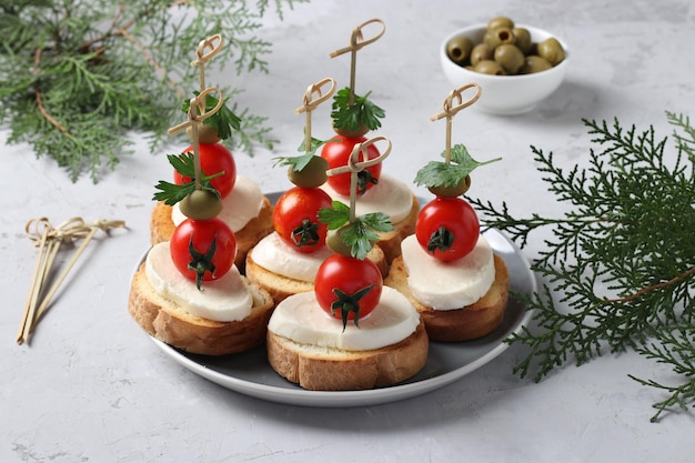 Foto canapeetjes van mozzarella, kerstomaatjes, groene olijven, peterselie op croutons van witbrood op grijze achtergrond feestelijke nieuwjaarssnack