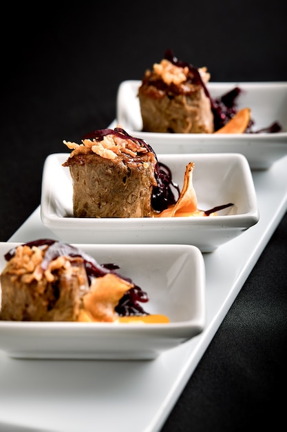 Canapes beef rolls with pumpkin sauce, on white plates