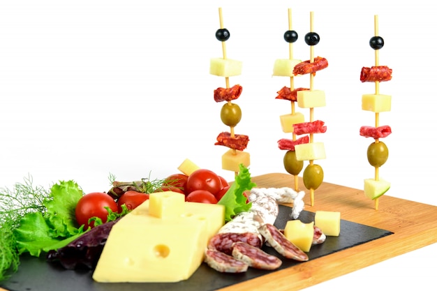 Canapes of olives, chorizo, salami, cheese and apple on the wooden sticks. Snack products on the tapas board.