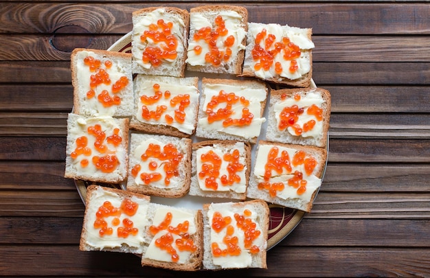 Canapes with cream cheese and caviar on white toast, on a plate on a wooden background