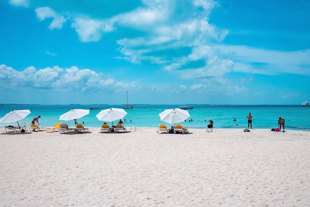 Cancun, mexico. may 30, 2021. deckchairs under canopy shade for resting on beach sand in front of sea with yachts. tourists enjoying beach holiday