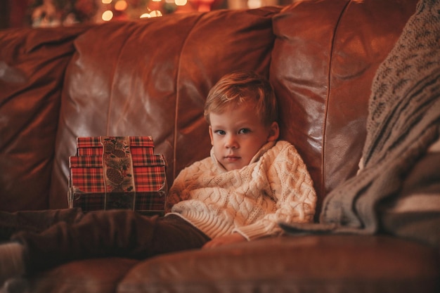 Откровенный подлинный счастливый маленький мальчик в вязаном бежевом свитере дурачится в украшенном рождественском домике