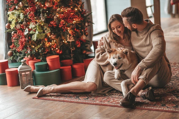 Счастливая супружеская пара проводит время вместе с японской собакой в рождественском домике