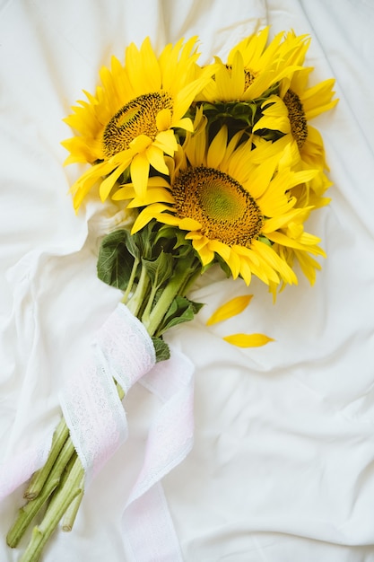 패브릭 흰색 배경에 솔직한 정통 노란 해바라기 꽃다발. 하얀 침대 시트에 노란 해바라기 꽃다발이 있는 배경. 화창한 날, 여름 꽃 개념입니다.