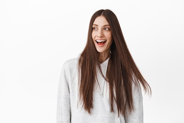 Candid girl laughs while long healthy hair flying in air Woman looking aside left at promo deal and smiling checking out something cool standing over white background