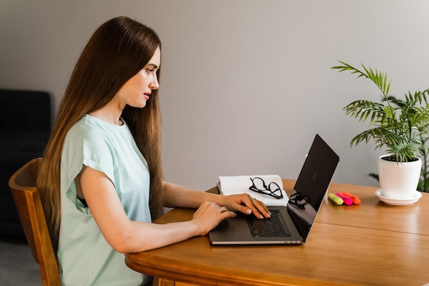 Candid girl with laptop is sitting on sofa smiling at\
successful work in it company cheerful young woman programmer works\
remotely on laptop and try to meet deadline at home