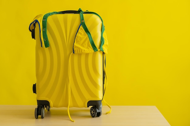 A candid minibikini of the coloring of the Brazilian flag hangs on a suitcase on a yellow background The concept of a summer beach holiday A woman is going on a trip to the sea