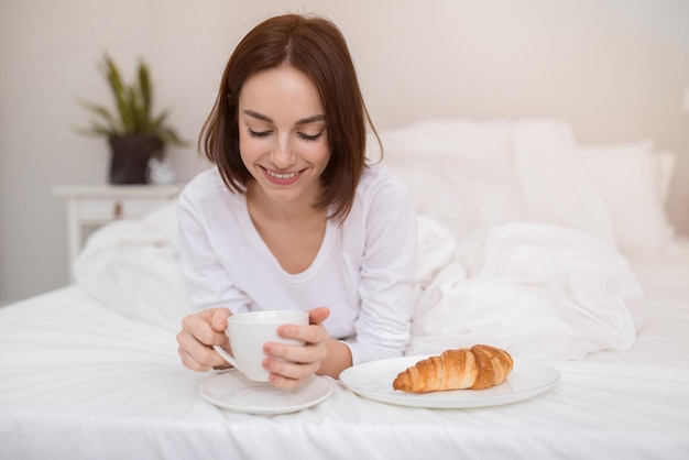 陽気な若い女性の率直な写真は、ベッドで朝食をとります