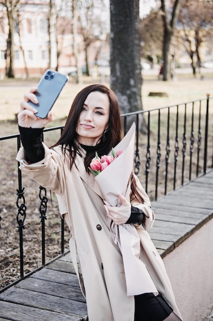 Candid portrait of happy woman with tulips bouquet taking selfie outdoors beautiful woman walking