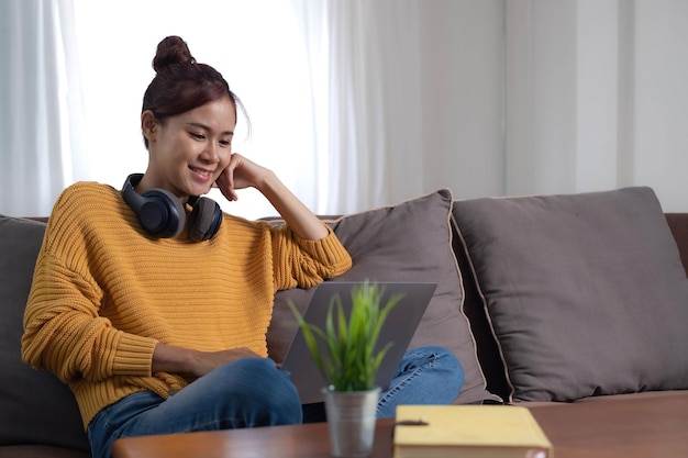 Candid van Aziatische vrouw die een laptop gebruikt om online films te kijken. Mobiel apparaat op de bank in de woonkamer. Jong gelukkig meisje dat geniet van entertainmentmedia online in het weekend.