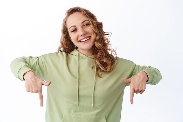 Candid woman smiling and showing advertisement on bottom, white wall