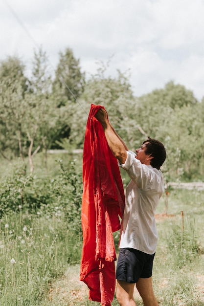 Candid young mature choring man chore homework and hanging the laundry to dry on a clothesline on the street in courtyard of village household cottage house summer freshness and laundry day