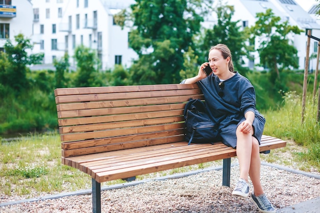Photo candid young woman talking by phone, sitting on a bench outside