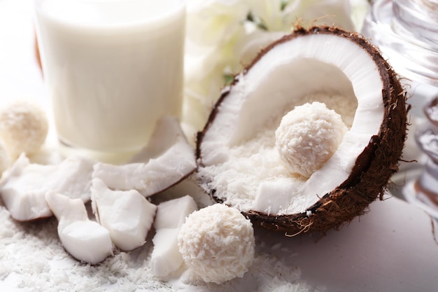 Candies in coconut flakes and fresh coconut on color wooden background