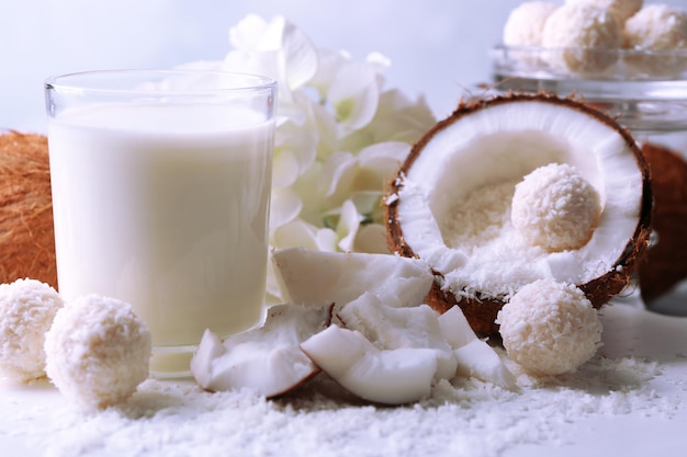 Candies in coconut flakes and fresh coconut on color wooden background