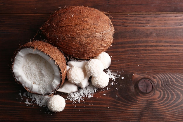 Candies in coconut flakes and fresh coconut on dark wooden background