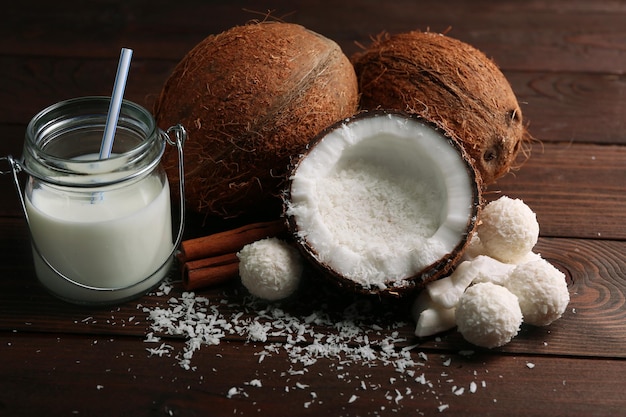 Candies in coconut flakes and fresh coconut on dark wooden background