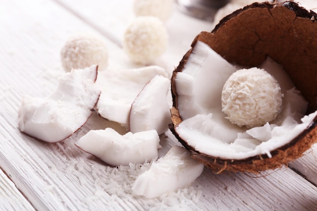 Candies in coconut flakes and fresh coconut on  light wooden background