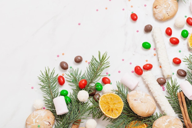 Candies and cookies with christmas tree branches on white marble background