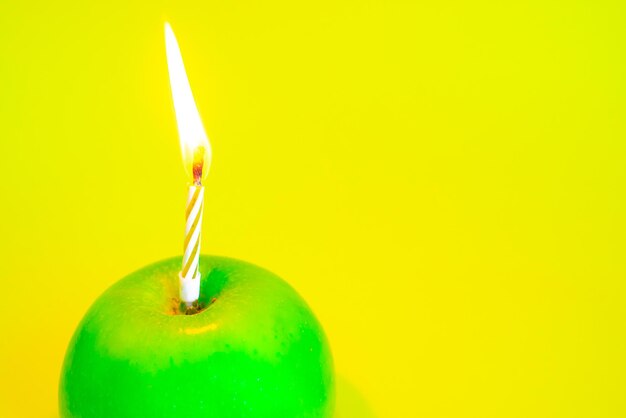 A candle burns in a green apple instead of a cake on a yellow background