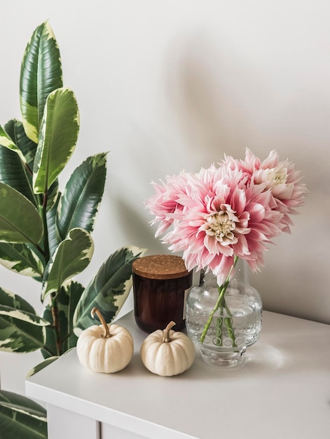 Candle decorative pumpkins bouquet of dahlias on a white chest of drawers in the living room interior