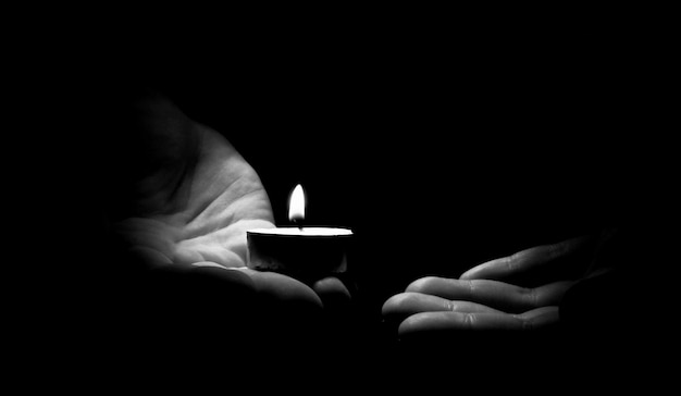 Photo candle in hand burning on the black background.