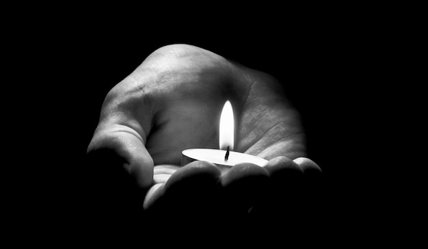 Candle in hand burning on the black background.