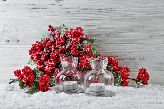 Candele e ramo di bacche di agrifoglio in una neve su sfondo di legno, still life