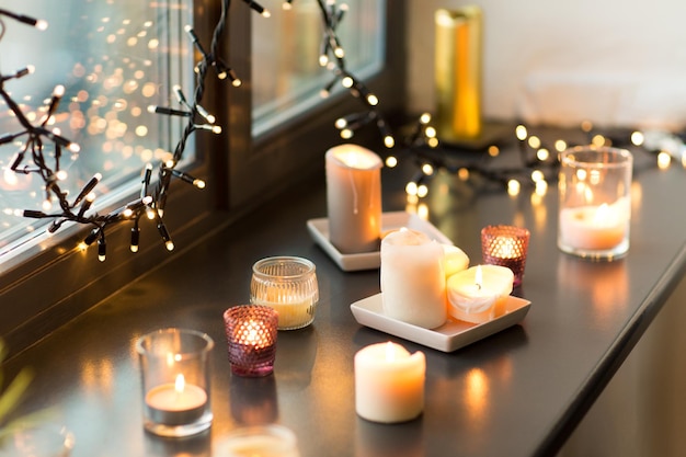 candles burning on window sill with garland lights