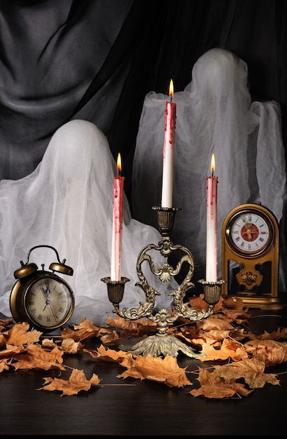 Candles among the fallen leaves with a clock and ghosts