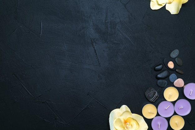 Candles, orchid flowers and pebbles on a black stone background. Top view, copy space. Spa concept, flat lay.