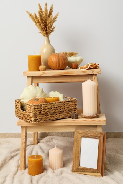 Candles and pumpkins on shelves photo frame and vase on beige background