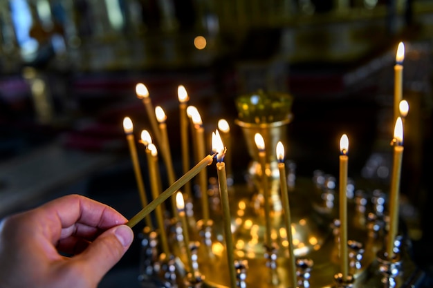 Candles in russian orthodox cathedral with icons on background\
hand putting candle