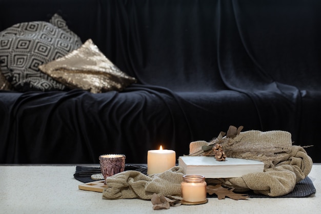 Candles, sweater and book on the table against the background of a dark sofa.