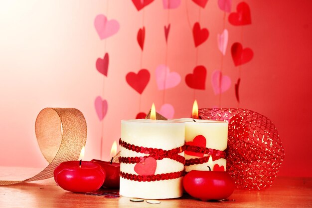 Candles for Valentine's Day on wooden table on red background