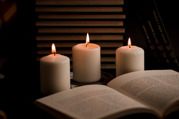 Candele con fiamma e libro di lettura sulla scrivania sfondo nero