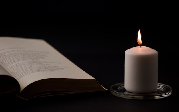 candles with flame and reading book on desk black background