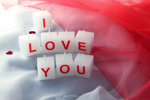 Candles with printed sign I LOVE YOU, on white fabric background