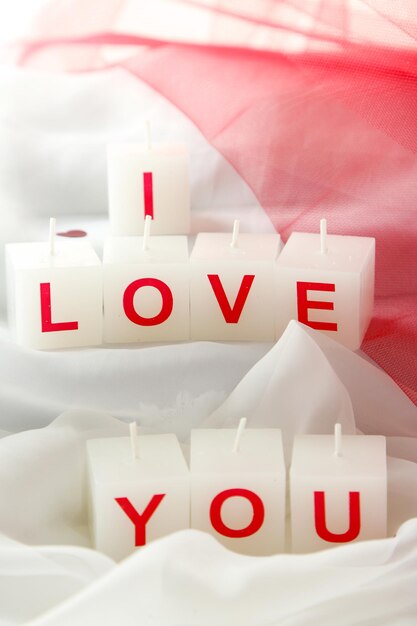 Candles with printed sign I LOVE YOU, on white fabric background