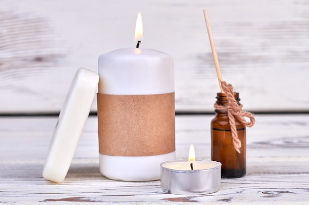 Candles with soap and oil bottle on white wooden background