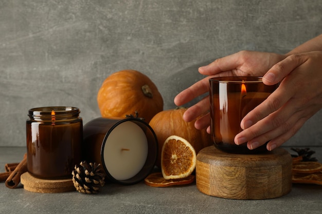 Candles on wooden stands pumpkins and female hands on gray background